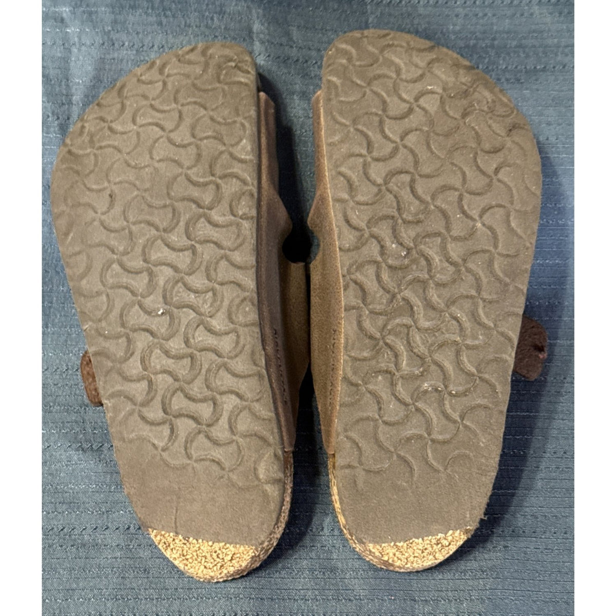 Bottom view of brown Birkenstock sandals showing worn tread and exposed cork at both heels.