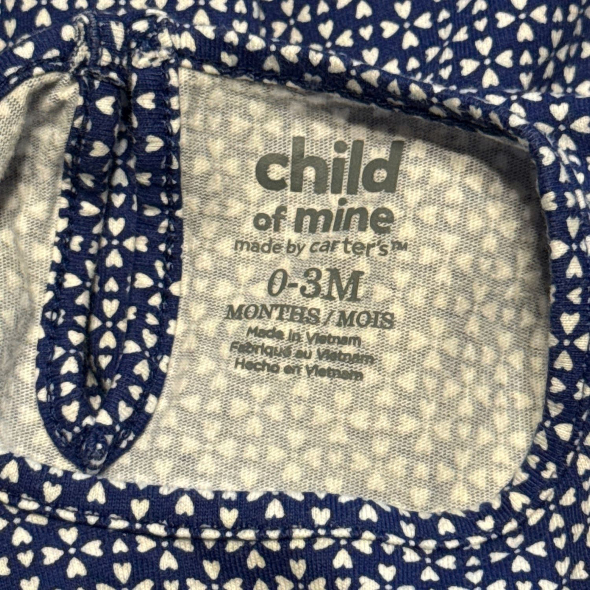 Carter's Child of Mine clothing label showing baby girls size 0–3 months on navy and white heart print fabric.