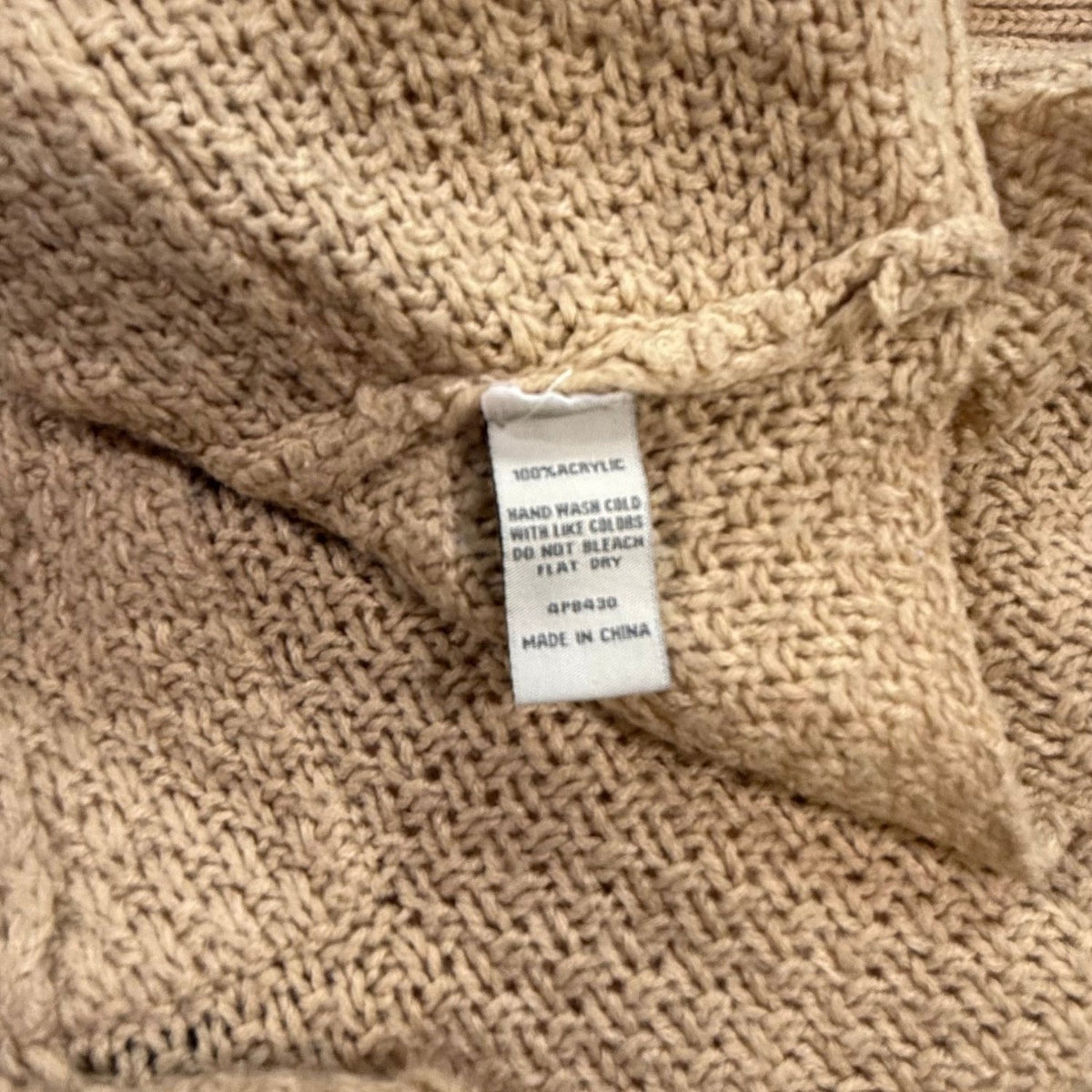 Material and care label on a beige Cecico cardigan showing 100% acrylic, hand wash cold, and flat dry instructions.