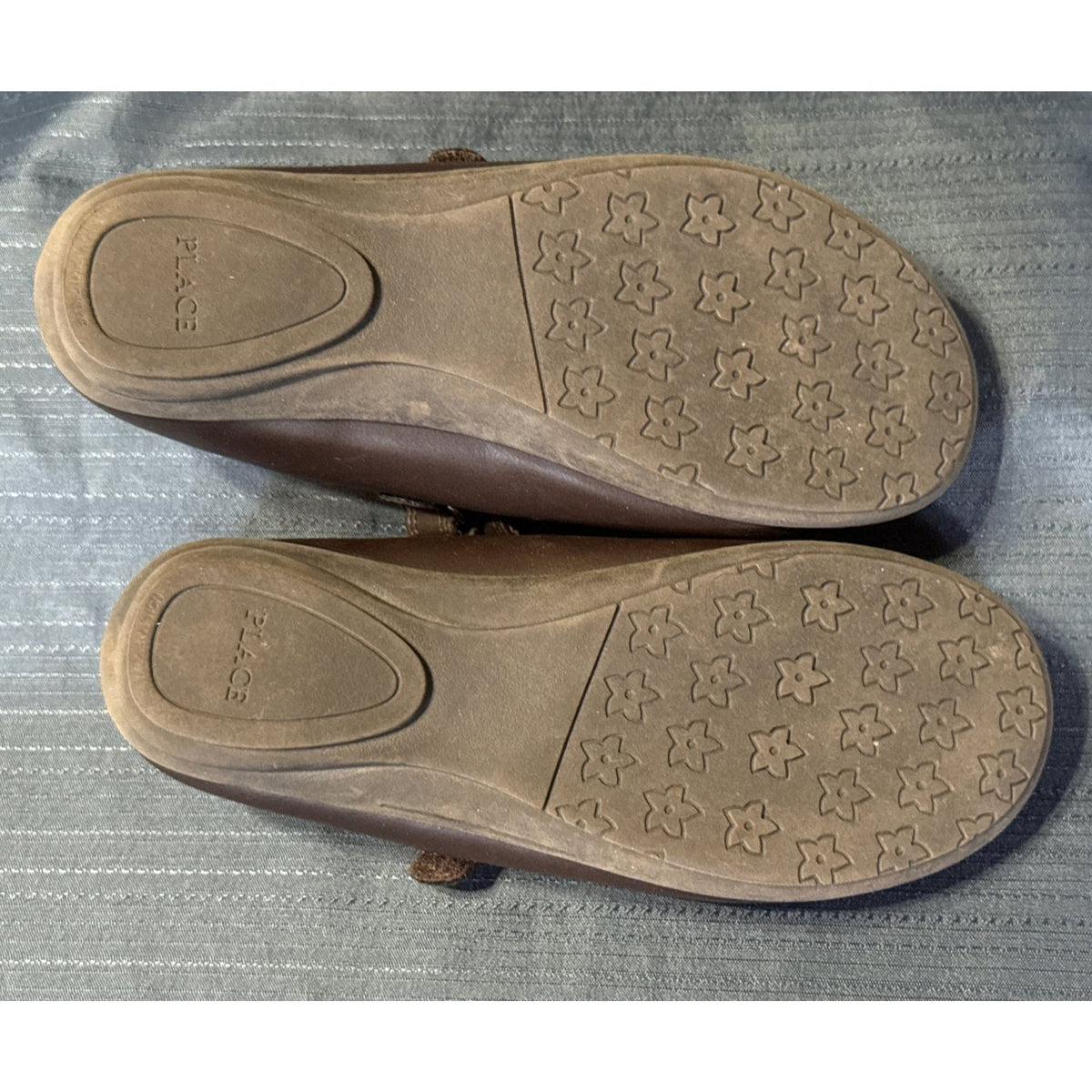 Bottom view of both brown Mary Jane shoes showing flower-patterned tread and wear.
