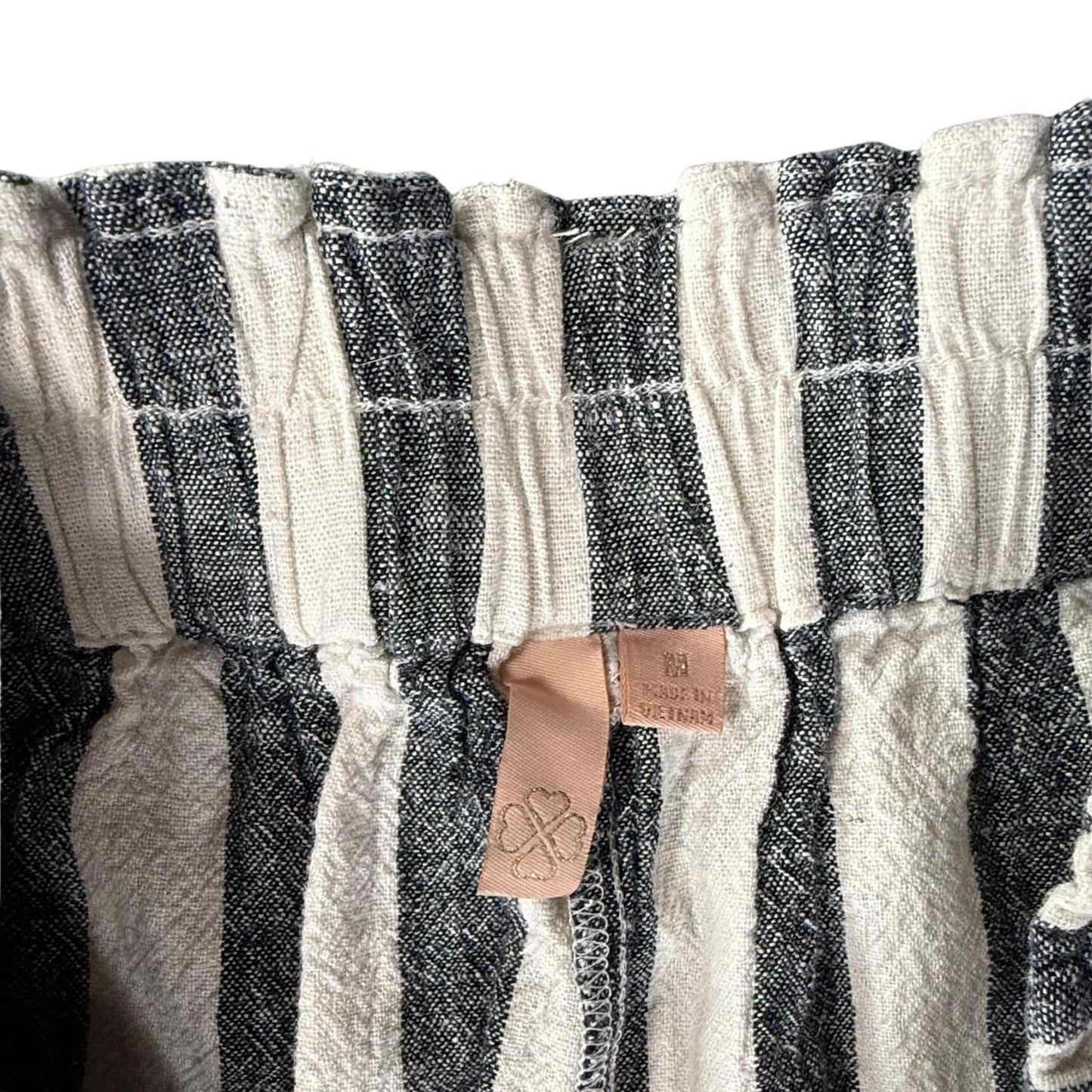 Pink clothing tag with clover leaf gold stitching on striped linen pants