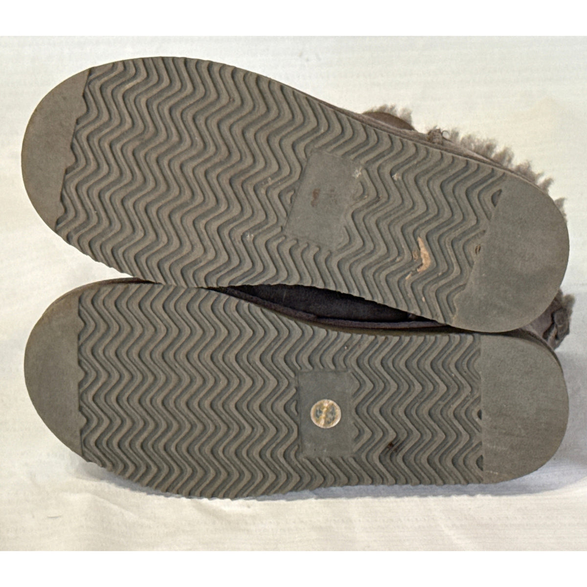 Bottom view of Member's Mark gray sheepskin short boots showing textured outsoles, visible tread wear, and a circular insert on one sole.