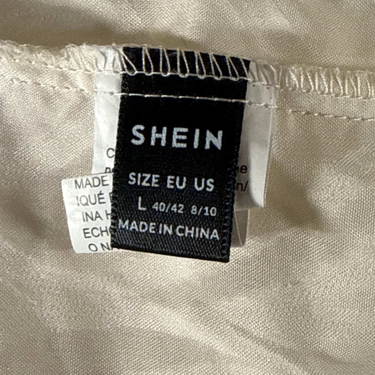 Close-up of black SHEIN clothing label showing size L, EU 40/42, and US 8/10.