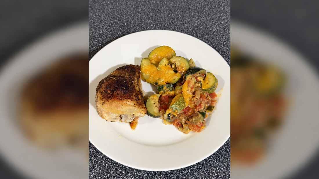 Plate of seasoned chicken with zucchini tomato cheddar skillet on a softly blurred matching background