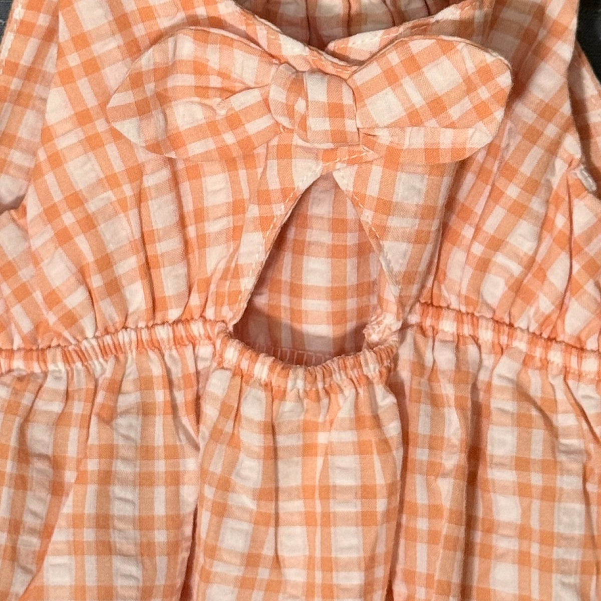 Close-up of oversized gingham bow and back keyhole opening on Carter's orange and white baby romper.