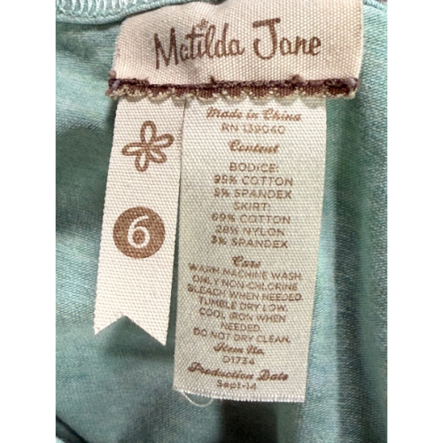 Close-up of a Metilda Jane clothing tag on a teal fabric background