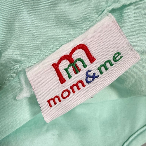 Close-up of a 'mom & me' label on a light green fabric background