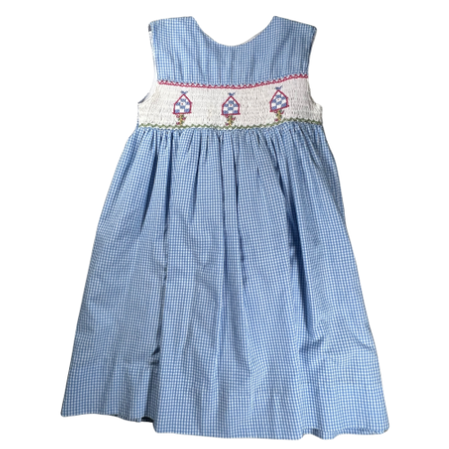 Pre-Owned blue and white gingham smocked dress for little girls, size 4, from Our Families Attic. Features white smocking, birdhouse embroidery, and a sleeveless design with a cross-over closure on the back. Light stain on the front.