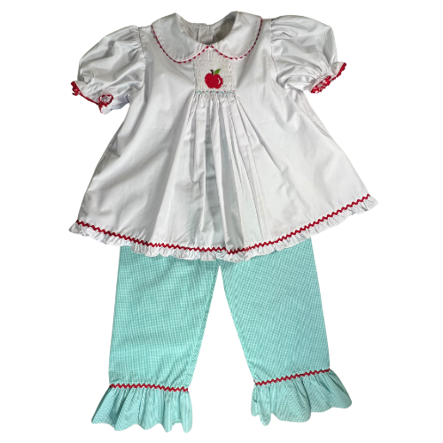 Charming pre-owned outfit by Shrimp & Grits Kids featuring an embroidered apple smock top with puffy sleeves and a five-button back, paired with green gingham pants with rickrack trim. Made from a soft polyester-cotton blend, it's in excellent condition and perfect for adding a playful touch to any wardrobe. Find at www.ourfamiliesattic.com