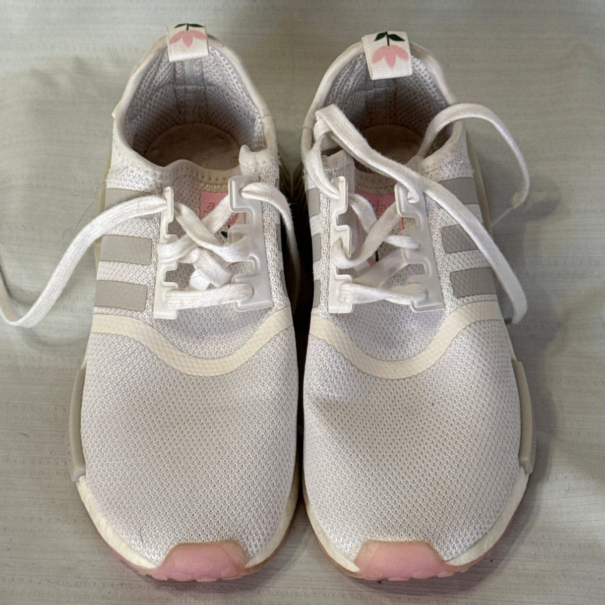 Front view of white Adidas NMD_R1 sneakers with white laces, gray stripes, and pink toe accents.