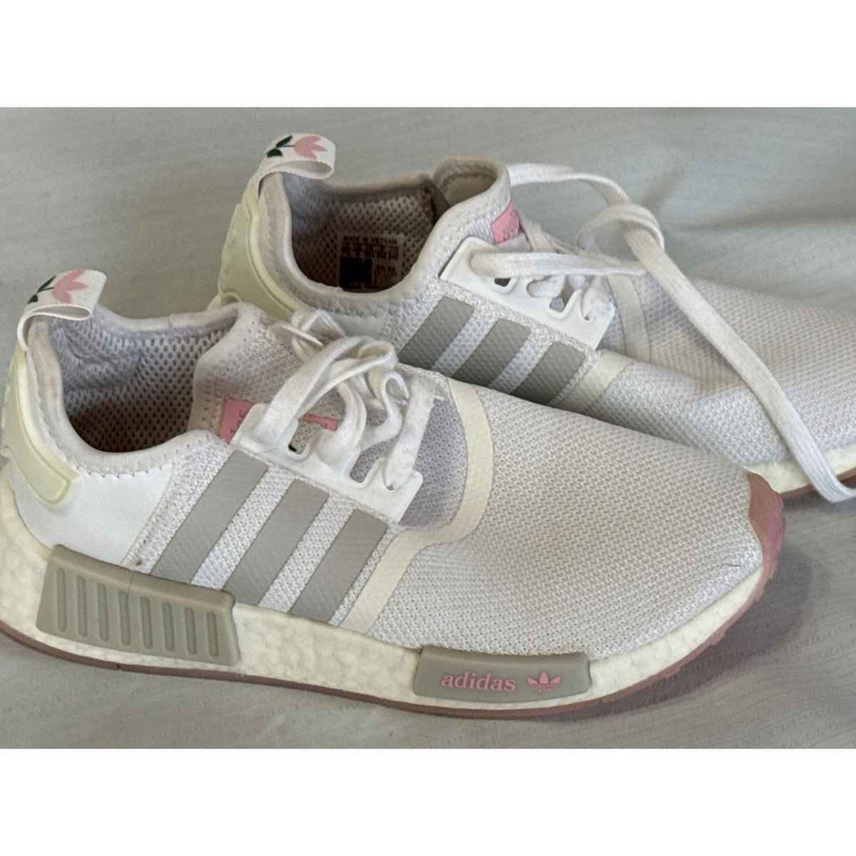 Side view of Adidas NMD_R1 sneakers showing mesh uppers, gray stripes, and midsole blocks with pink branding.