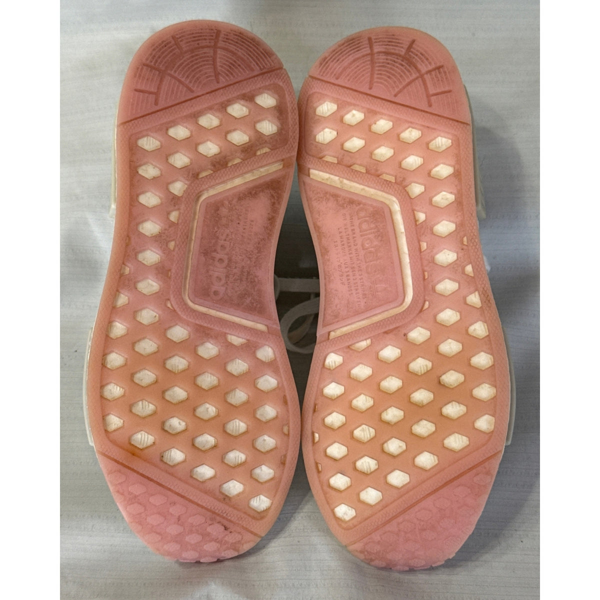 Bottom view of both Adidas NMD_R1 sneakers showing pink outsoles with visible dirt and wear.