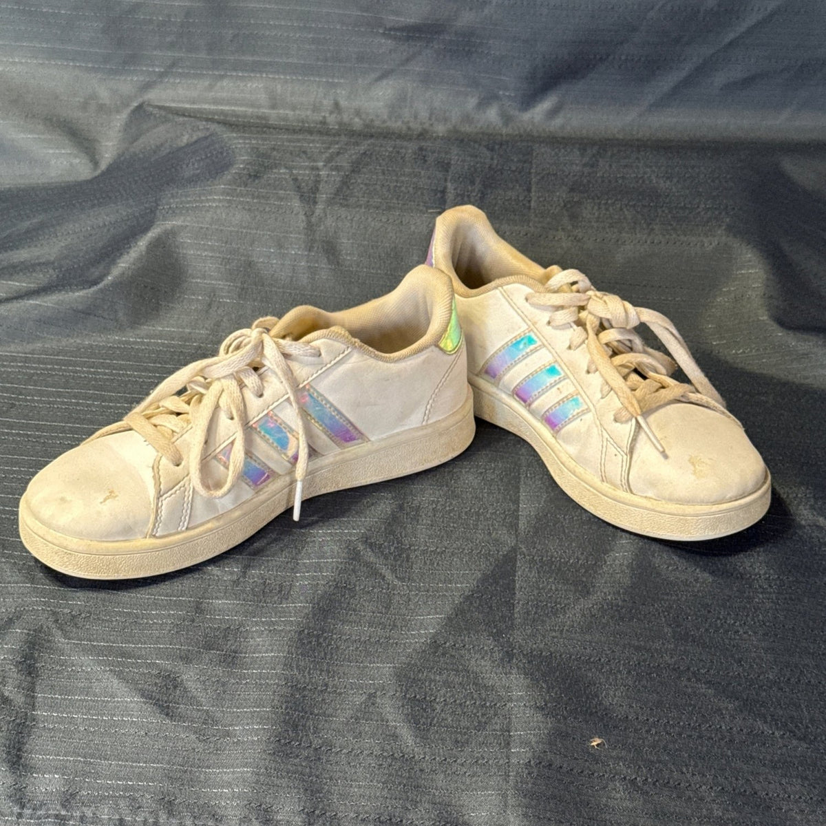 Angled view of white Adidas lace-up sneakers with iridescent stripes and visible toe marks.
