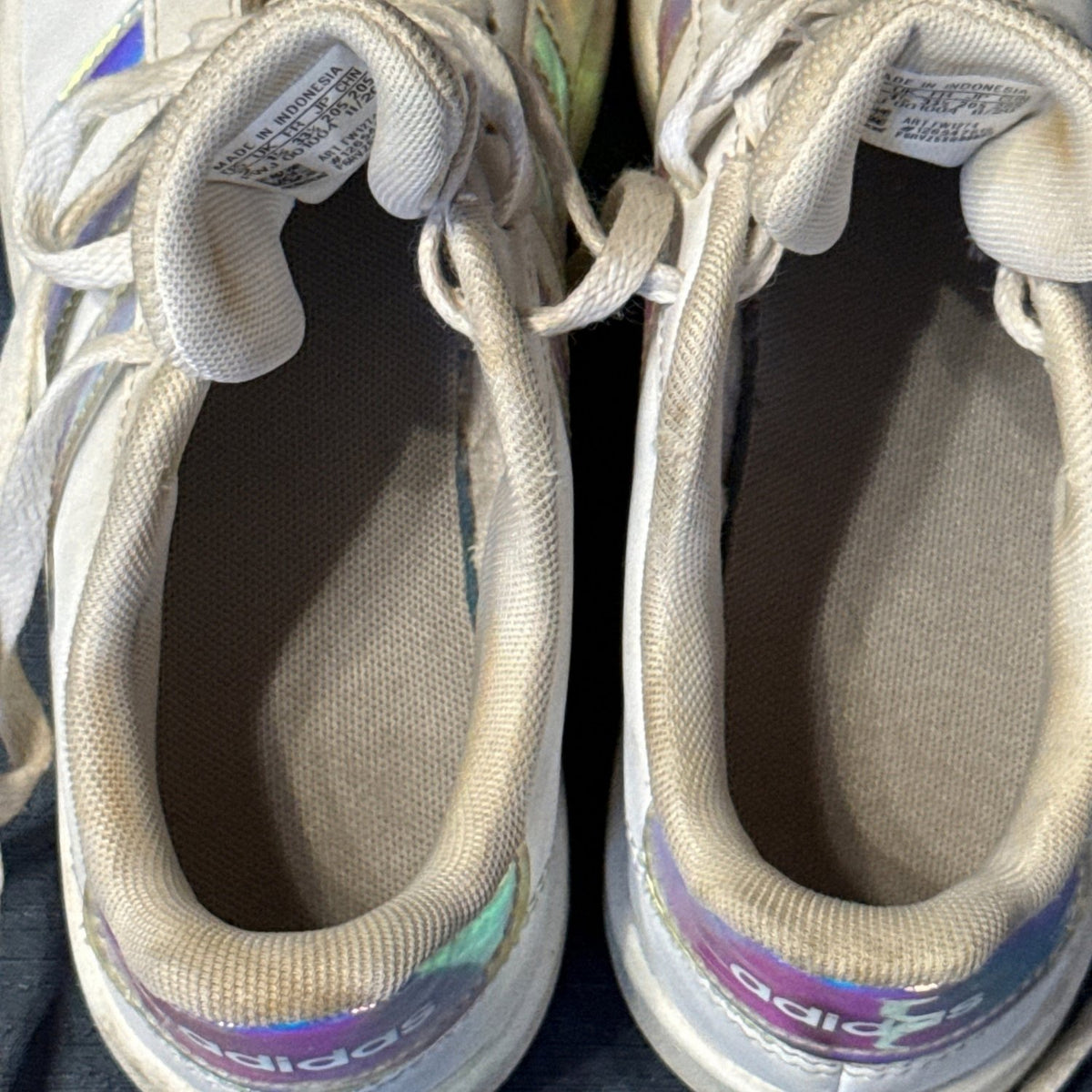Interior view of white Adidas sneakers showing fabric lining, insoles, and visible discoloration.
