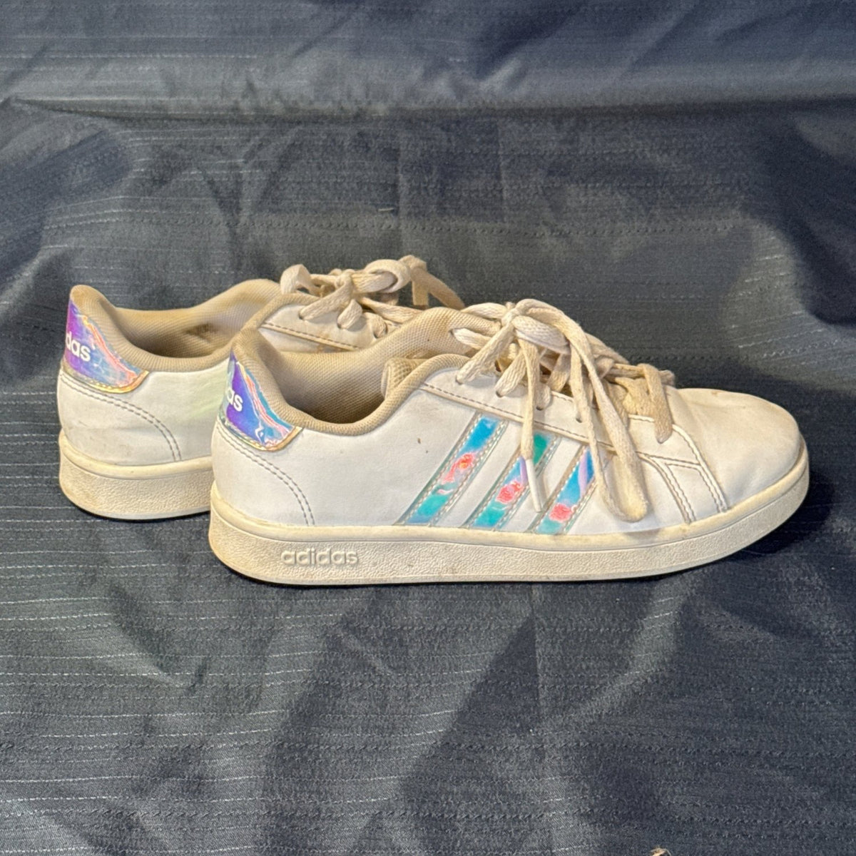 Side view of white Adidas low-top sneakers with iridescent three-stripe accents and heel tabs.
