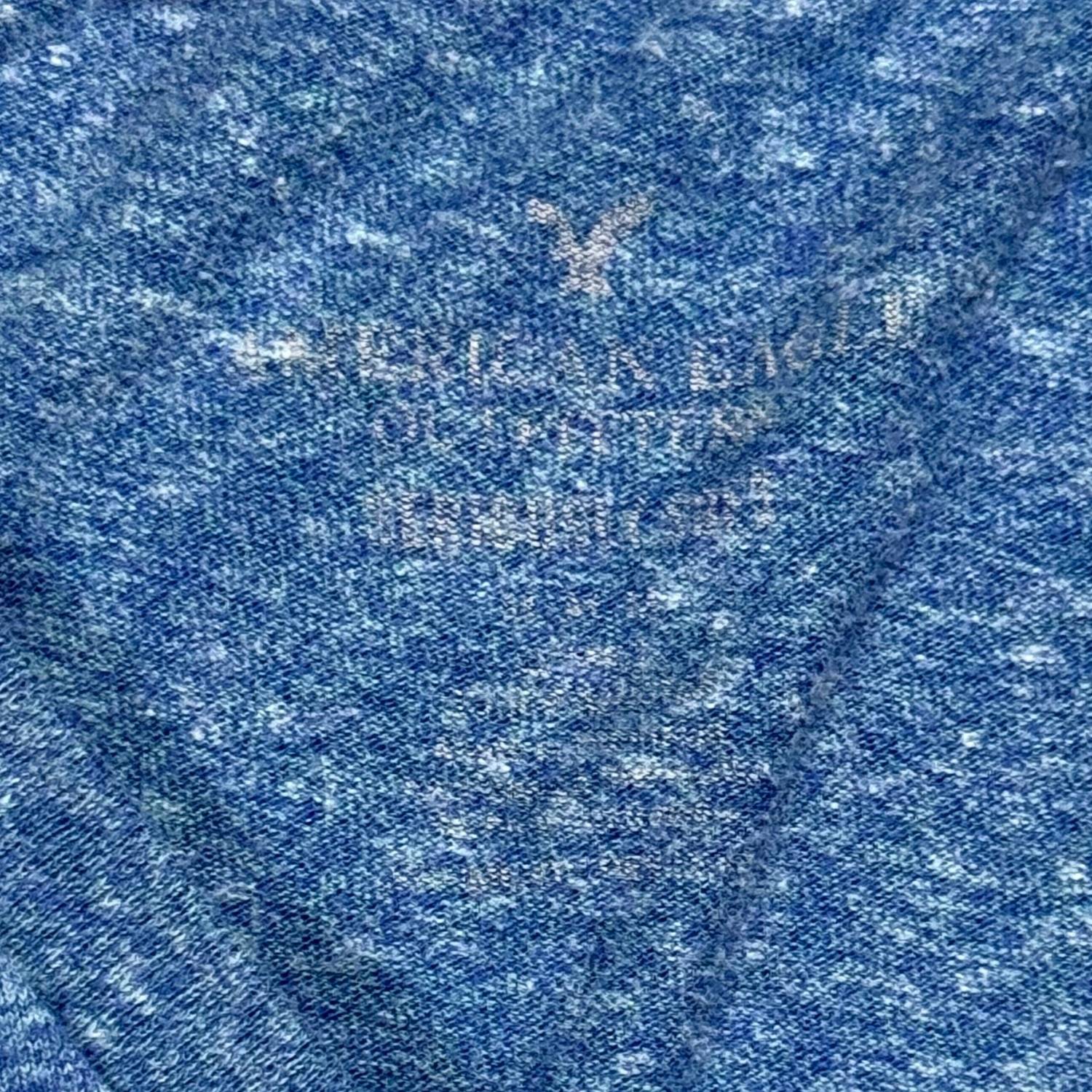 Close-up of heather blue fabric with a faded American Eagle brand logo.