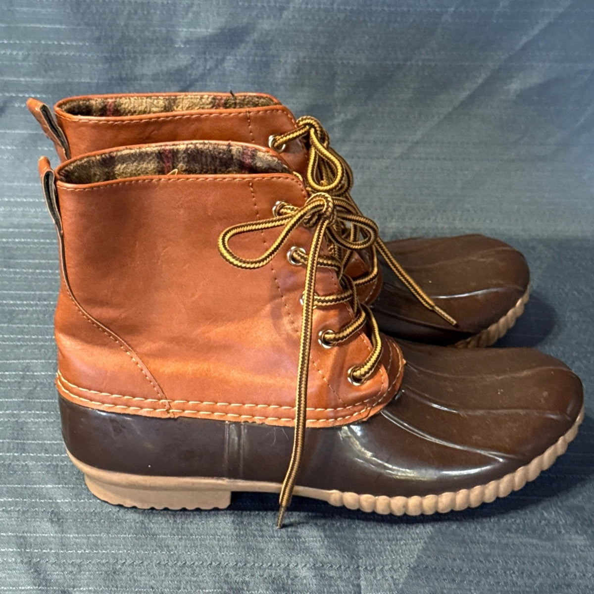 Side profiles of brown ANNA lace-up duck boots with dark brown rubber bottoms and tan soles.