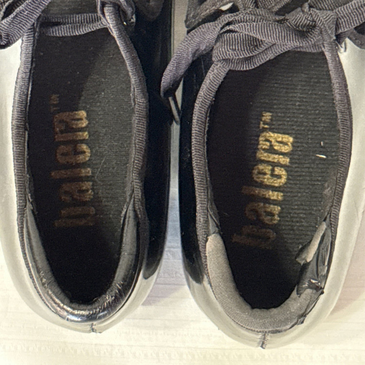 Overhead close-up of Balera tap shoes showing worn insoles and peeling around the heel openings.
