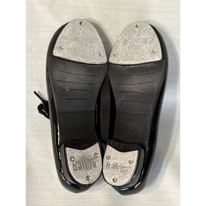 Bottom view of black Balera tap shoes showing textured rubber soles and worn metal toe and heel taps.
