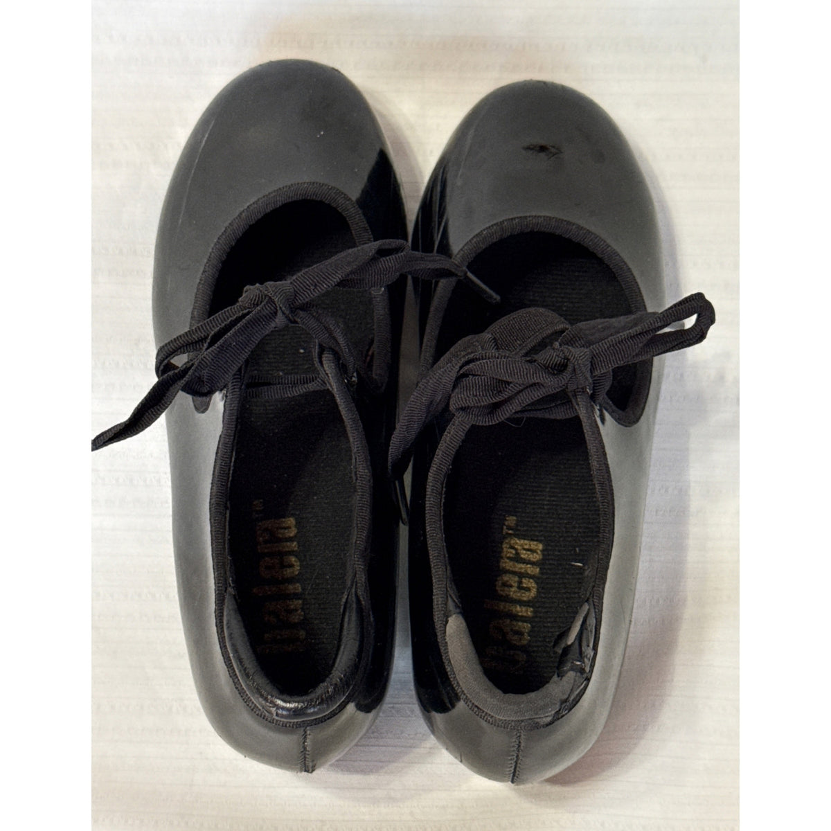 Top view of black Balera tap shoes showing tie laces, elastic instep straps, and heel-opening wear.

