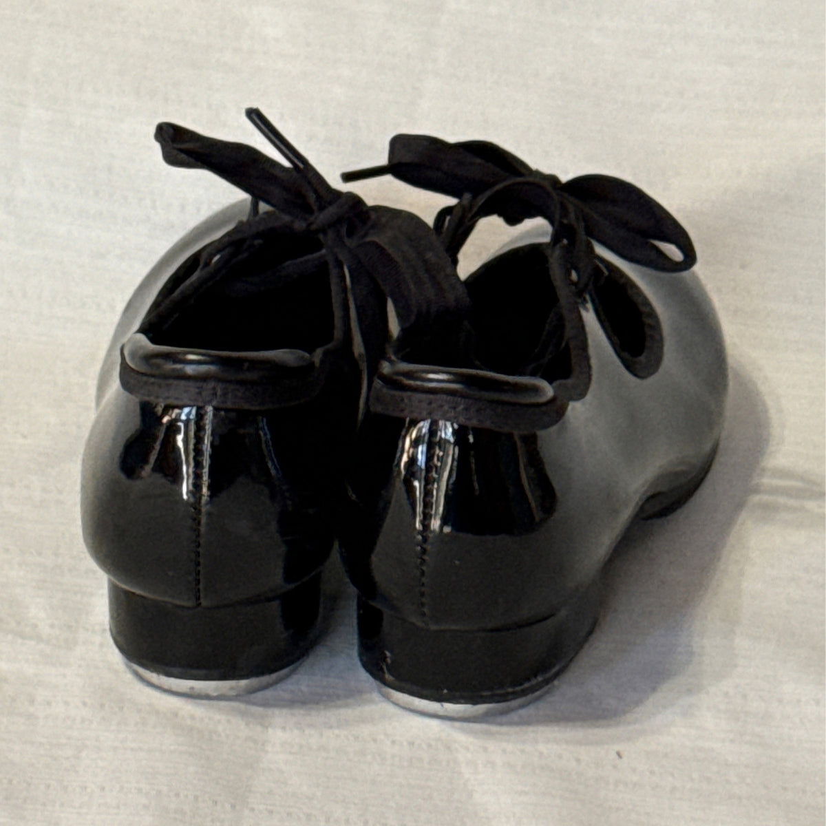 Back view of Balera black tap shoes showing heel seams, glossy uppers, and low block heels.
