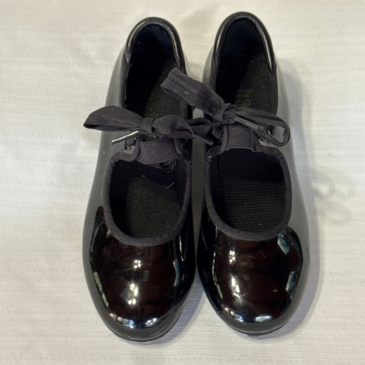 Front view of Balera black tap shoes showing rounded toes, bow ties, and elastic instep straps.