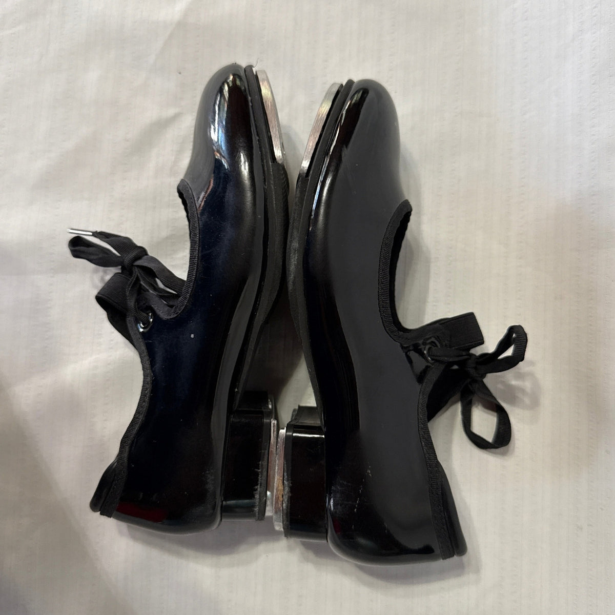 Outer side view of Balera black tap shoes showing scratches and scuffs on the glossy uppers.
