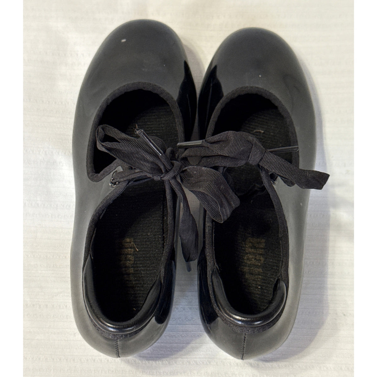 Top view of Balera black tap shoes showing bow ties, shoe openings, and worn insole branding.
