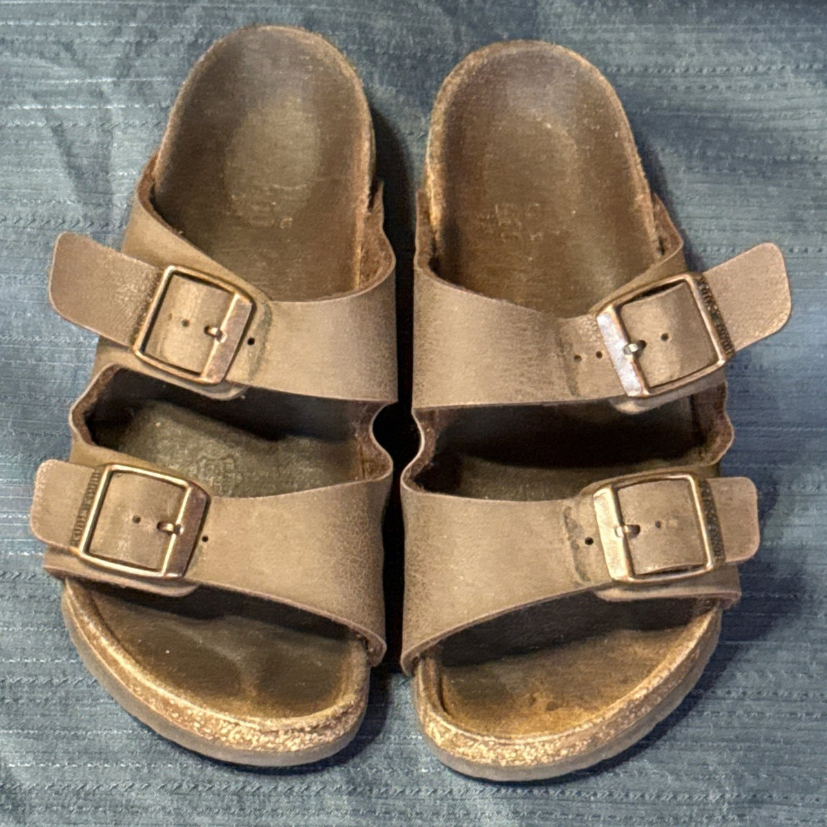 Front view of brown Birkenstock sandals showing open toes, buckle straps, and worn footbed edges.