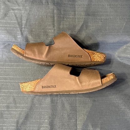 Side view of brown Birkenstock sandals showing branded uppers, contoured footbeds, and sole wear.
