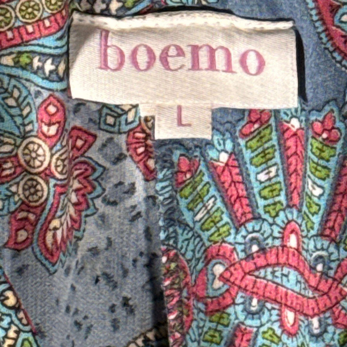 Close-up of Boemo clothing label marked size L against blue-gray fabric with colorful paisley and floral pattern.