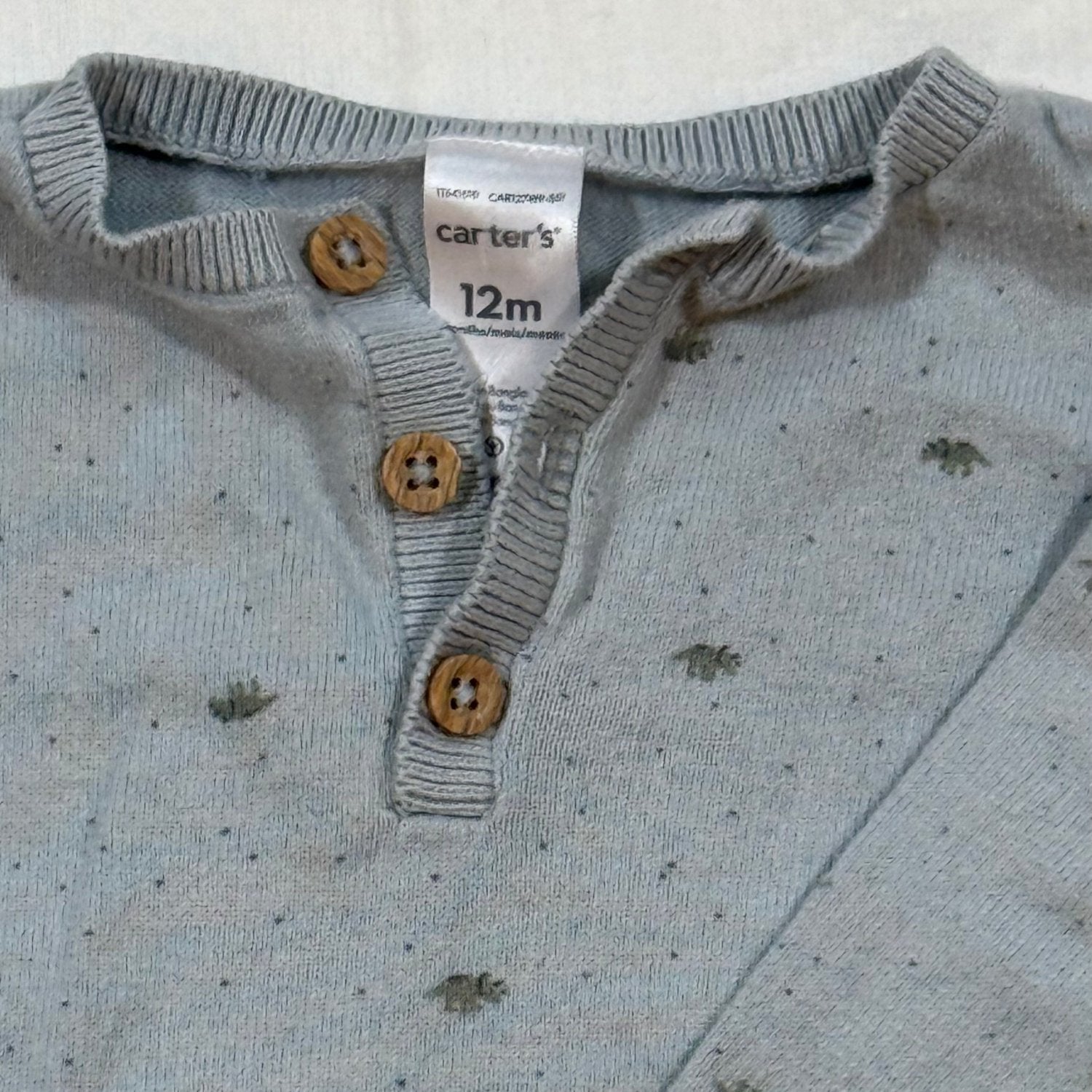 Close-up of Carter's 12 month dinosaur sweater Henley neckline with three wood-look buttons and size tag