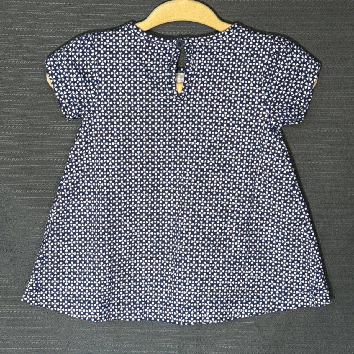 Back view of Carter's Child of Mine navy blue baby dress with white heart print, short sleeves, and button keyhole closure.