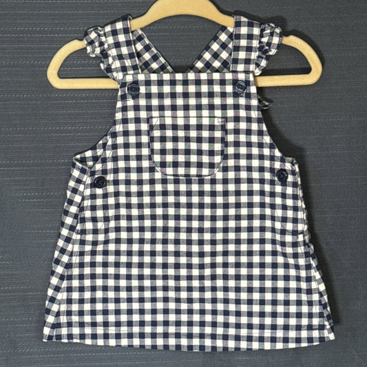 Front view of Carter's Child of Mine baby girls' gingham pinafore dress in navy blue and white, featuring ruffled shoulders, front pocket, and decorative buttons.