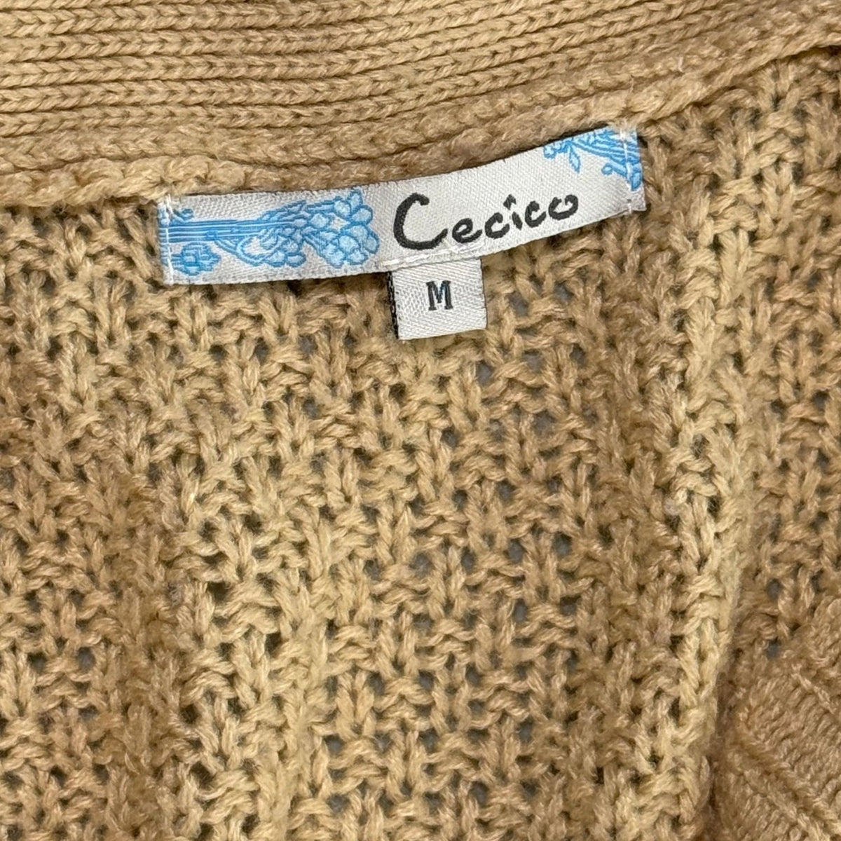 Cecico brand tag and medium size label against beige textured knit fabric.