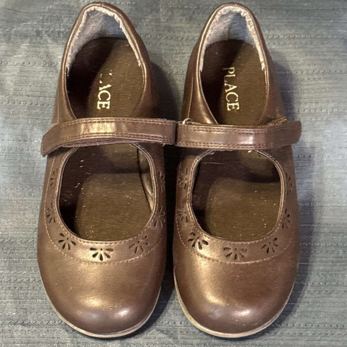 Top view of brown Mary Jane shoes showing adjustable straps, flower cutouts, and interior lining.