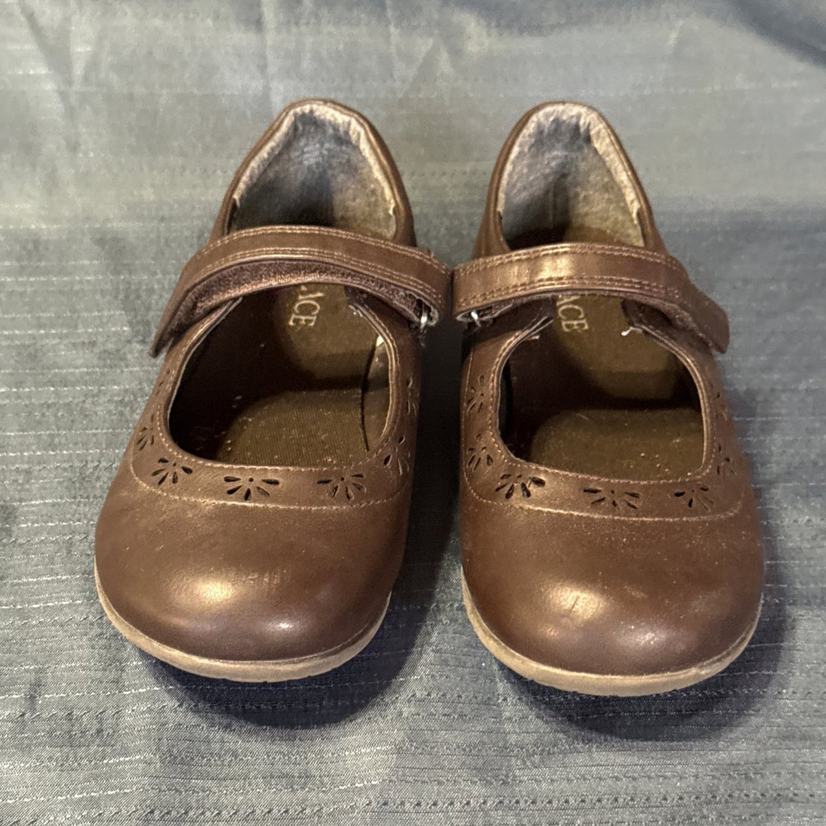 Front view of The Children’s Place girls’ brown Mary Jane shoes with rounded toes and flower-shaped cutouts.