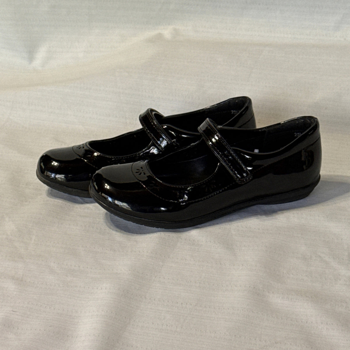 Left side view of girls’ black Mary Jane shoes showing rounded toes and decorative flower-shaped cutouts.
