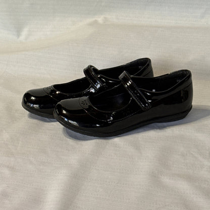 Left side view of girls’ black Mary Jane shoes showing rounded toes and decorative flower-shaped cutouts.
