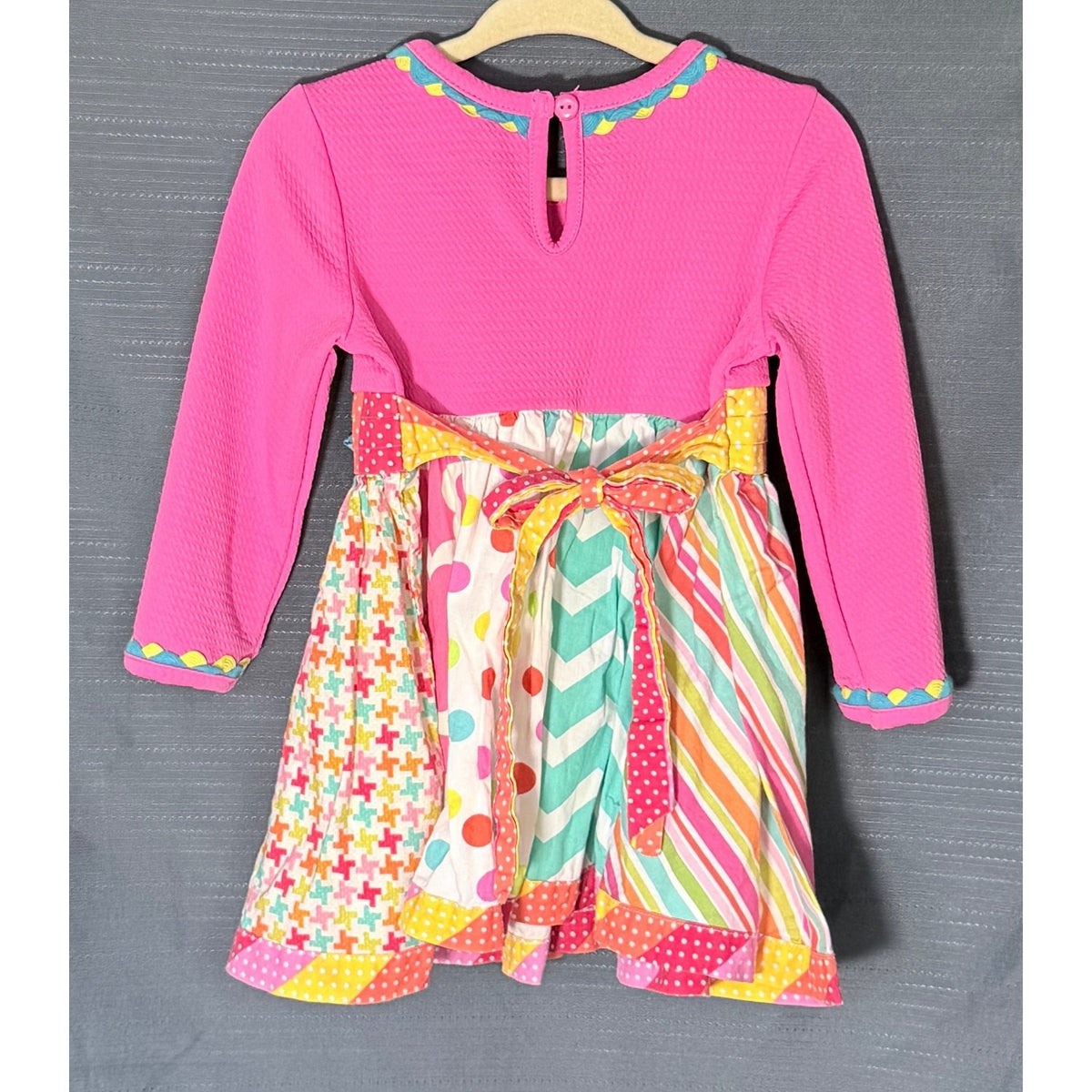Back view of Counting Daisies dress with bright pink long sleeves, multicolor patterned skirt, and ribbon waist tie.