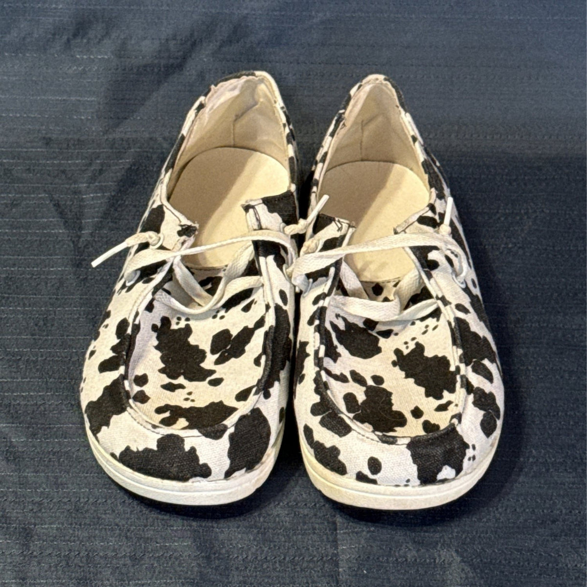 Front view of black-and-white cow-print shoes showing rounded toes, moc-toe stitching, and white laces.