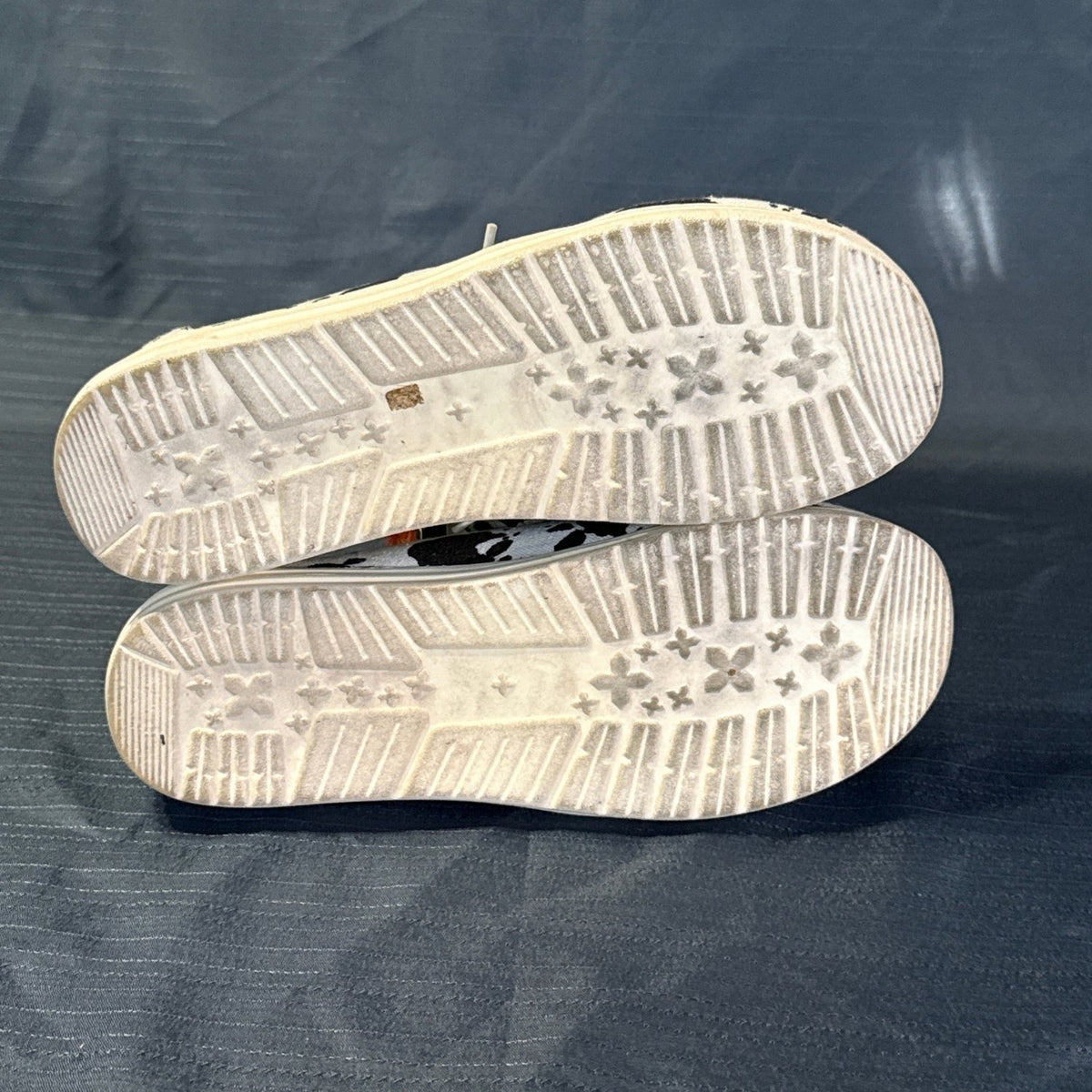 Bottom view of cow-print slip-on shoes showing patterned tread and discoloration on the light-colored soles.
