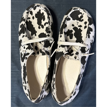 Top view of black-and-white cow-print canvas shoes with white laces and light-colored insoles.
