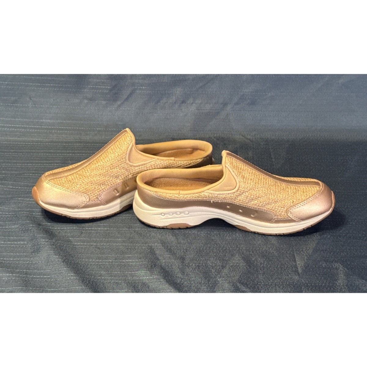 Side profiles of rose-gold Easy Spirit mule sneakers showing sparkly fabric uppers and open backs.
