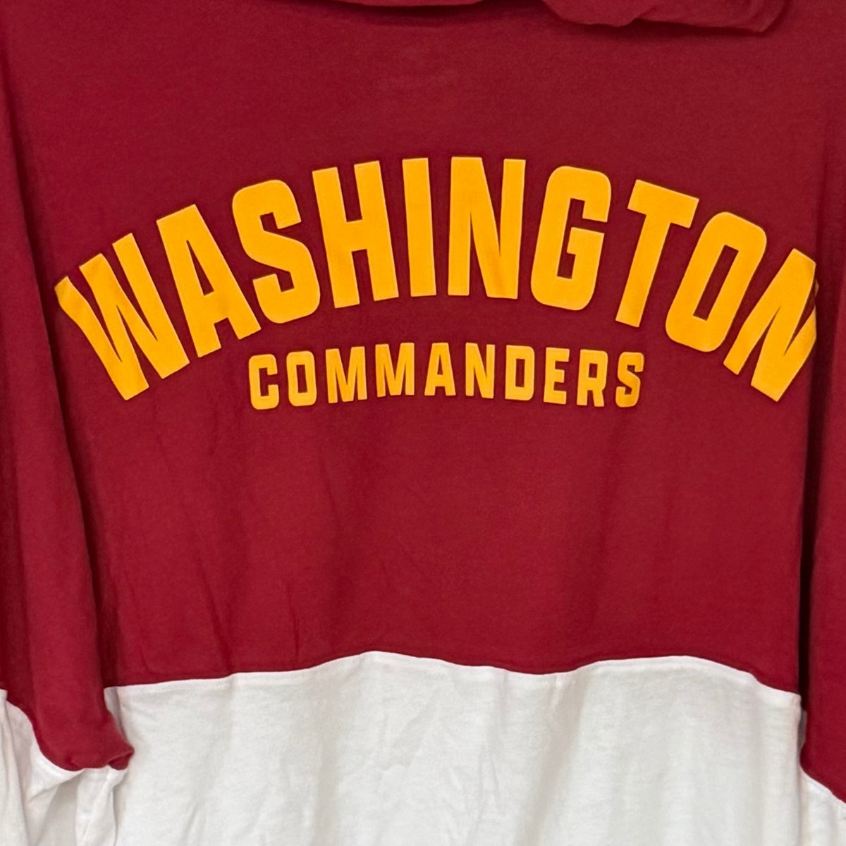 Close-up of gold Washington Commanders lettering across burgundy upper back of Fanatics hooded shirt.