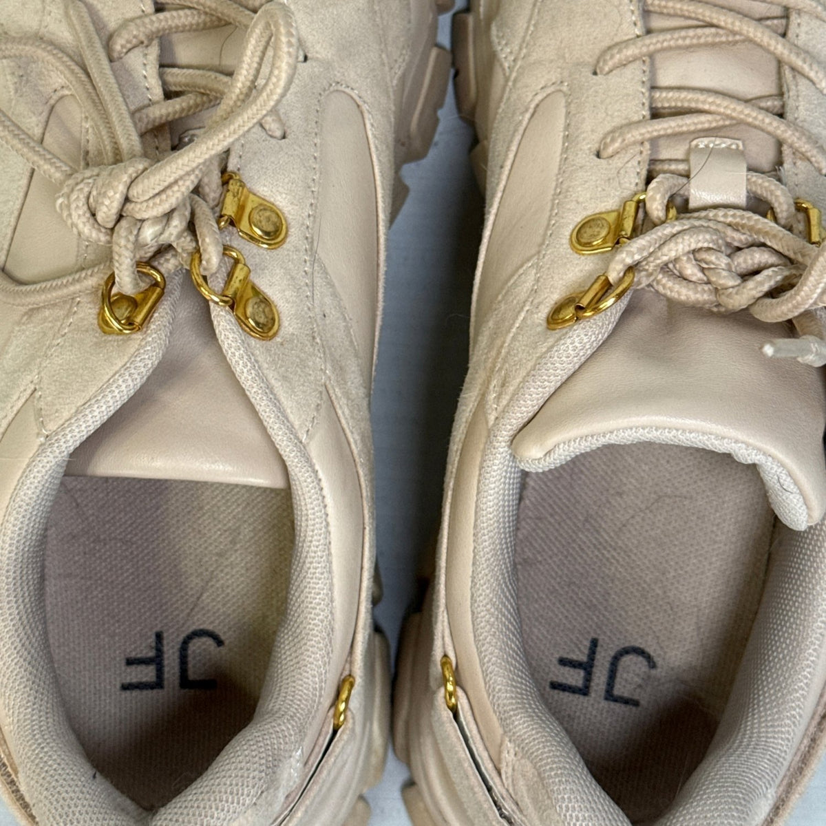 Close-up of JustFab Ximena sneaker interiors showing textile lining, branded insoles, and gold-tone lace hooks.