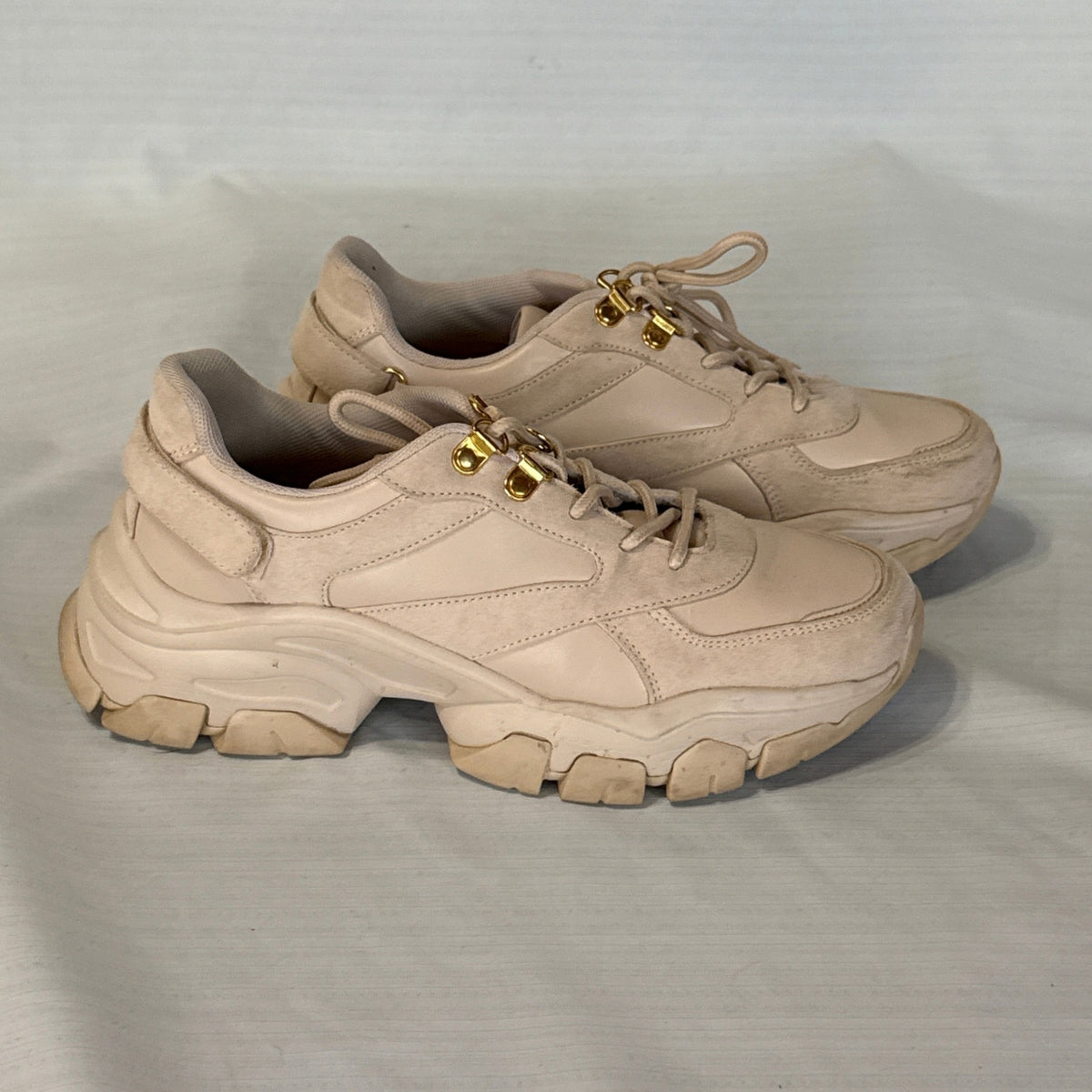 Side view of blush beige JustFab Ximena chunky sneakers showing mixed-texture uppers, gold-tone lace hooks, and sculpted soles.