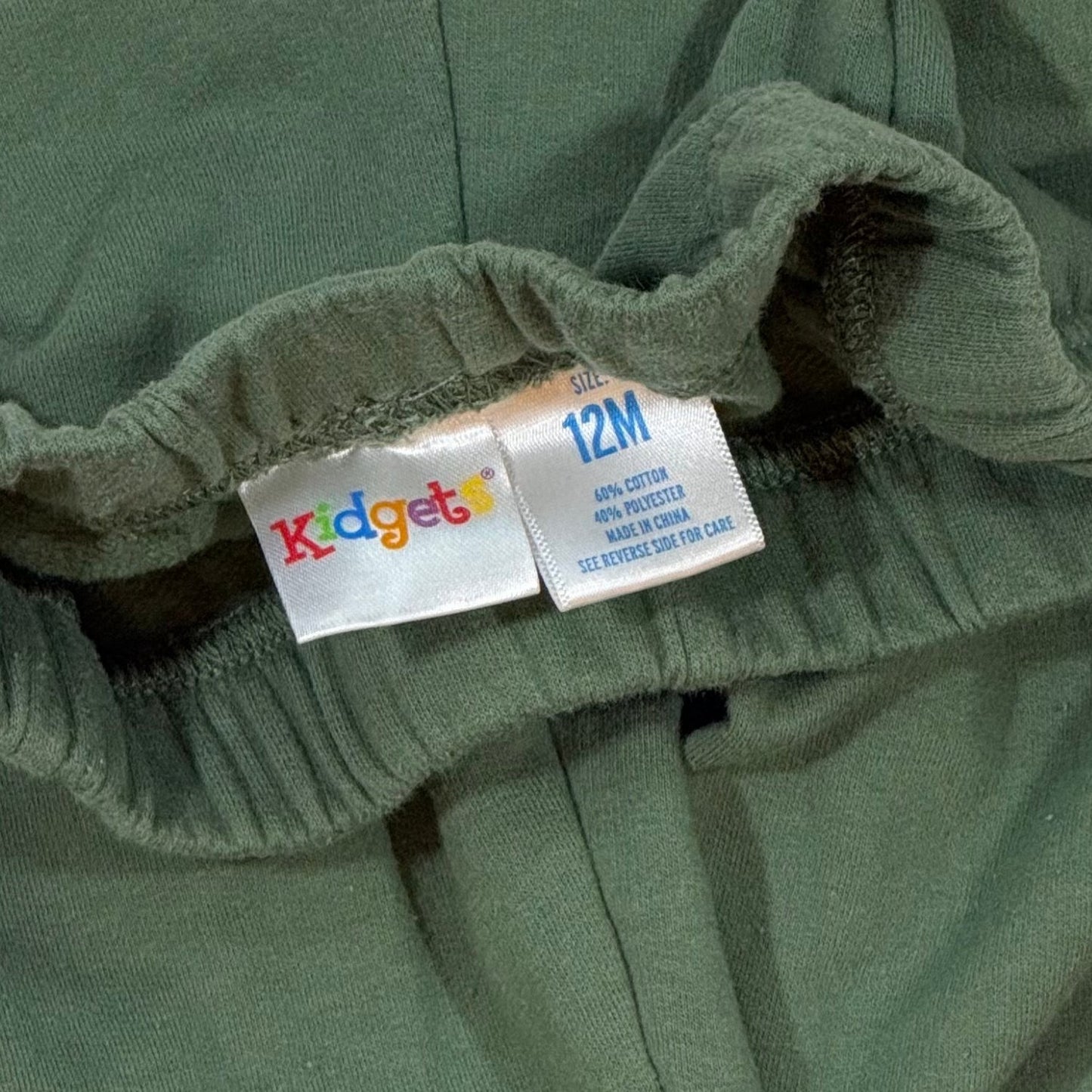 Kidgets baby clothing tag showing size 12 months and cotton polyester fabric blend