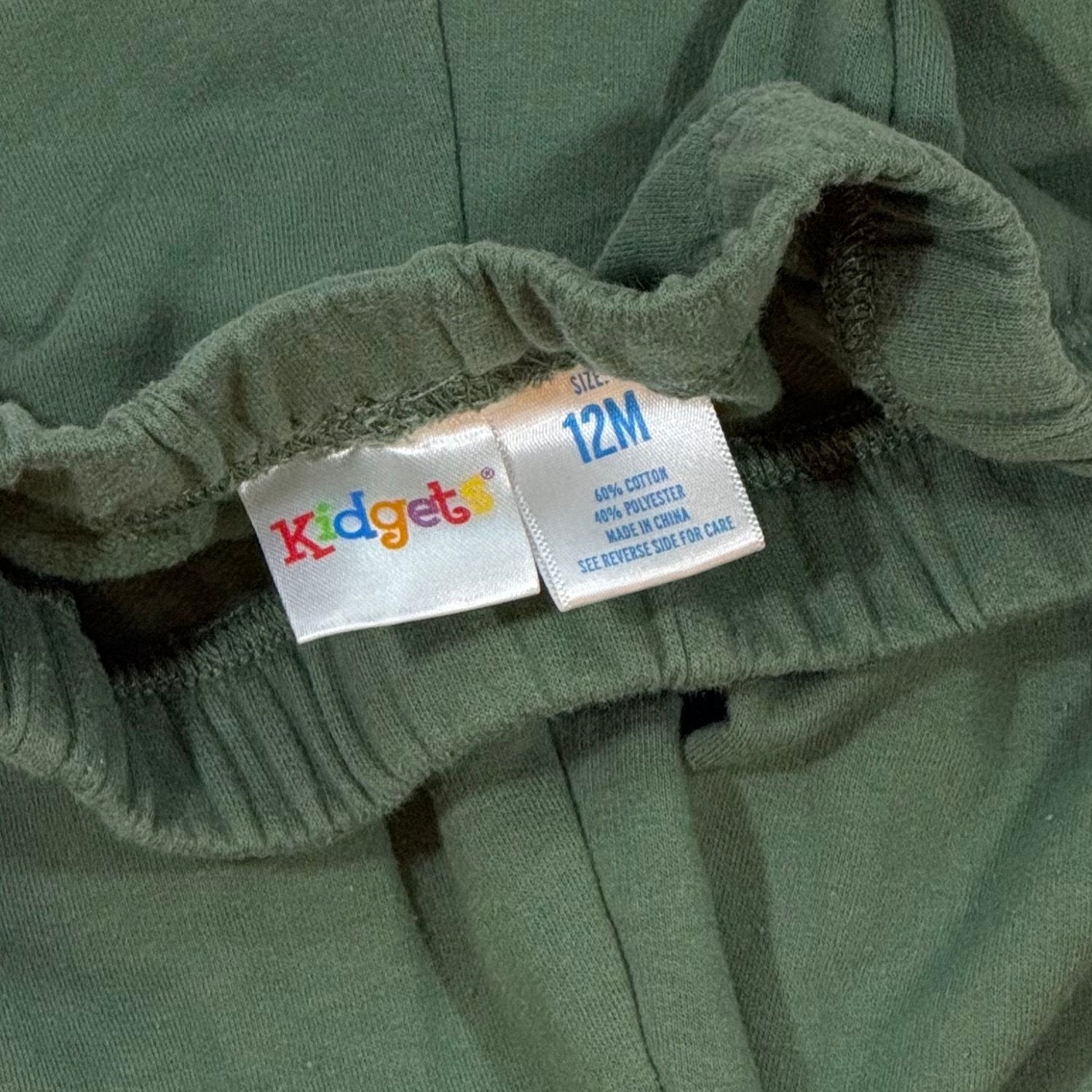 Kidgets baby clothing tag showing size 12 months and cotton polyester fabric blend