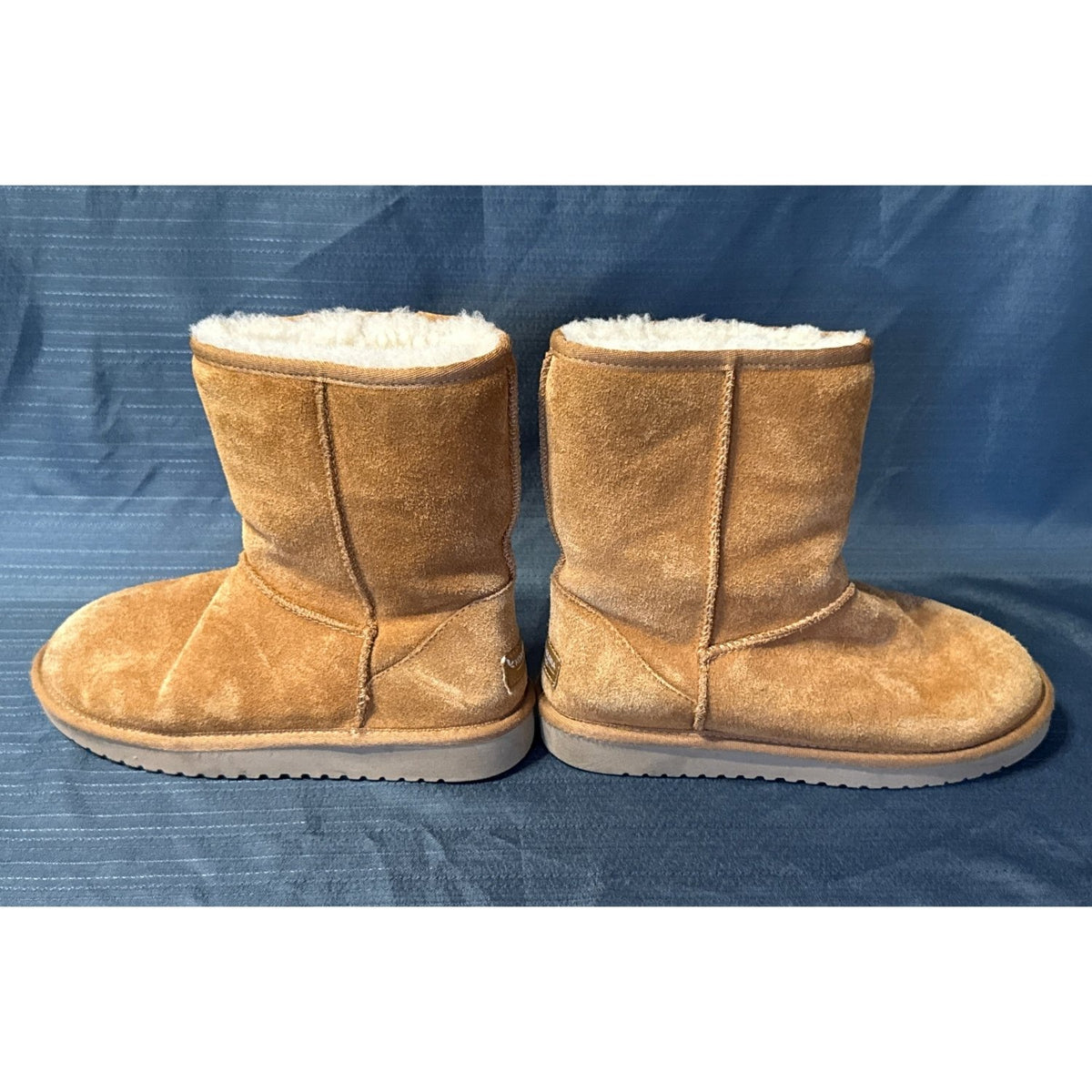 Inner side view of chestnut suede short boots showing exposed seams and flat soles.